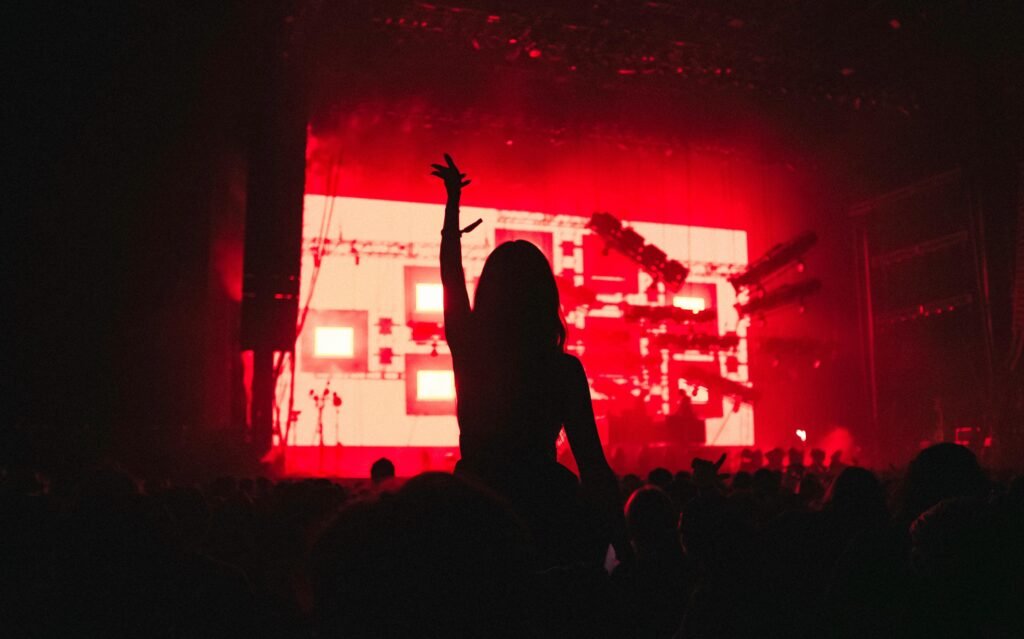 Silhouette of a woman raising her arm in a vibrant music festival with red lighting.